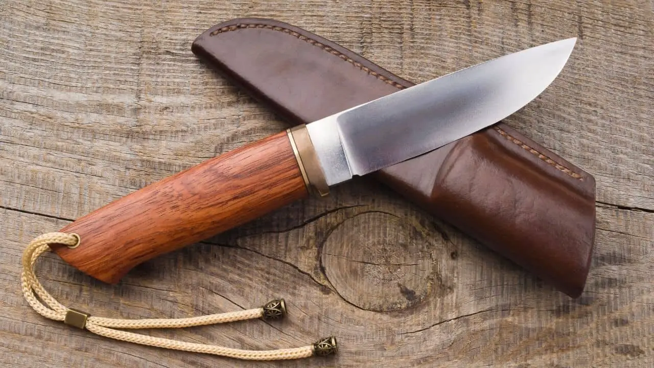 photo of a fixed blade knife with wooden handle and leather sheath on wood background