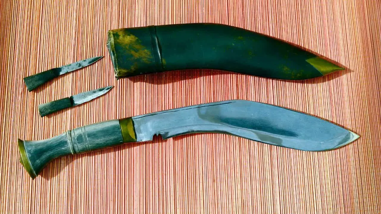 photo of a kukri knife and sheath laying on a striped surface with two smaller blades