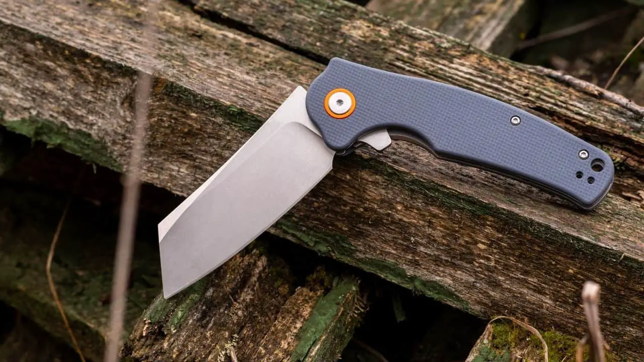 a photo of a gray and orange folding knife half open on a piece of wood