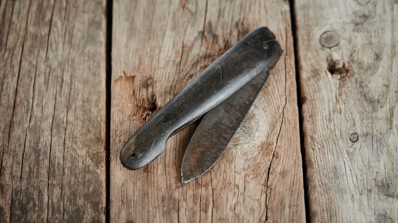 photo of a old rusty pocket knife half open on some wooden planks