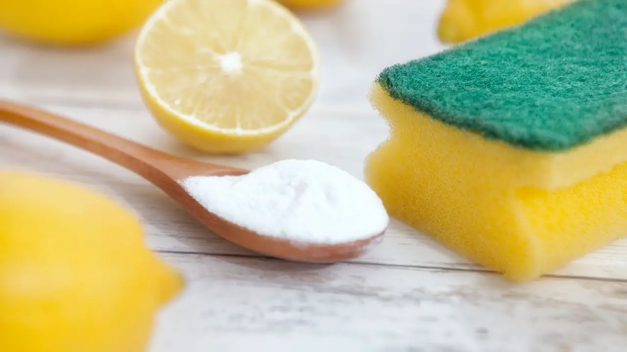 photo of a wooden spoon of baking soda next to a lemon and a sponge