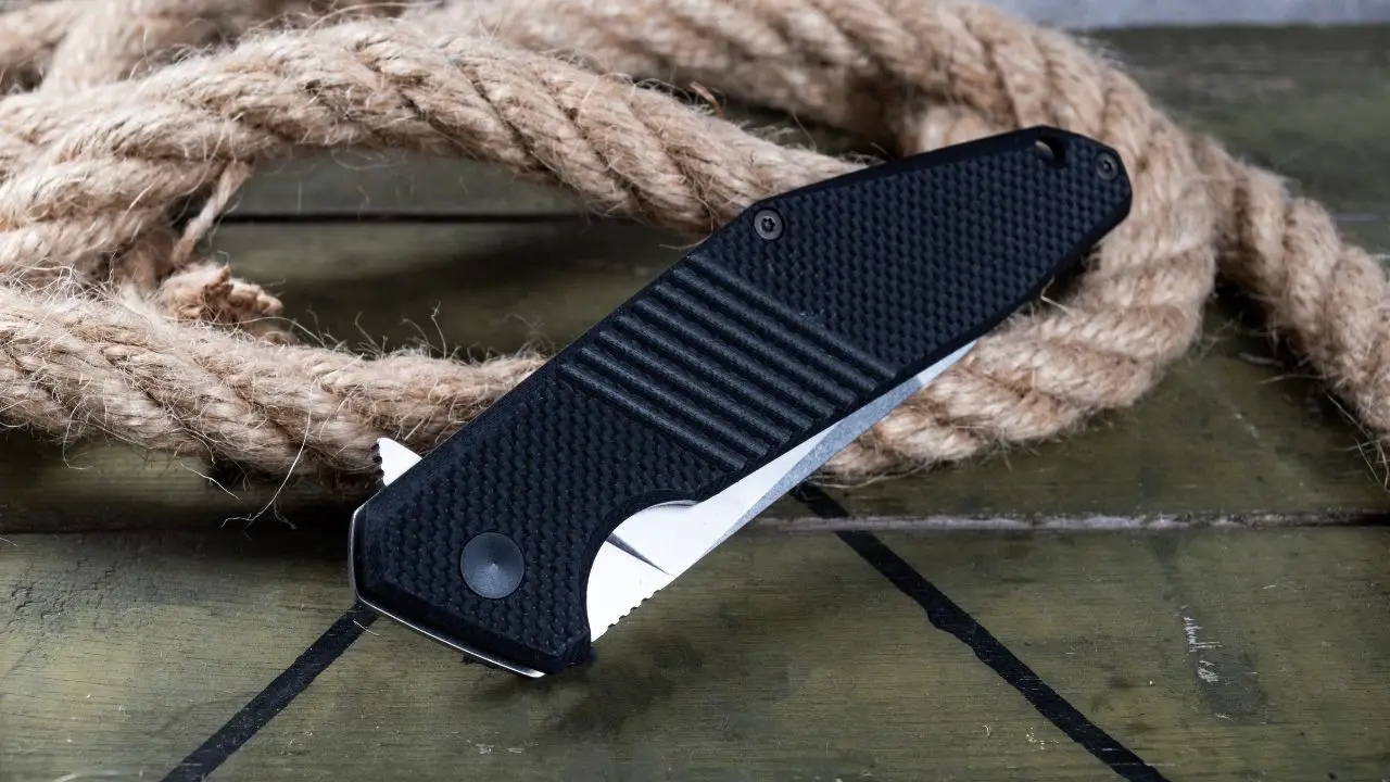 photo of a folding knife with black handle leaning against rope